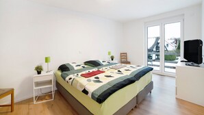 Un dormitorio con cama, mesita de noche, silla, televisor y vistas a través de un ventanal.