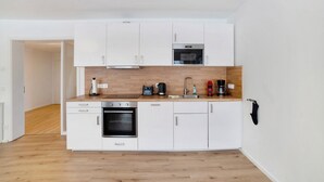 Una cocina compacta con armarios blancos, horno empotrado, microondas y cafetera.