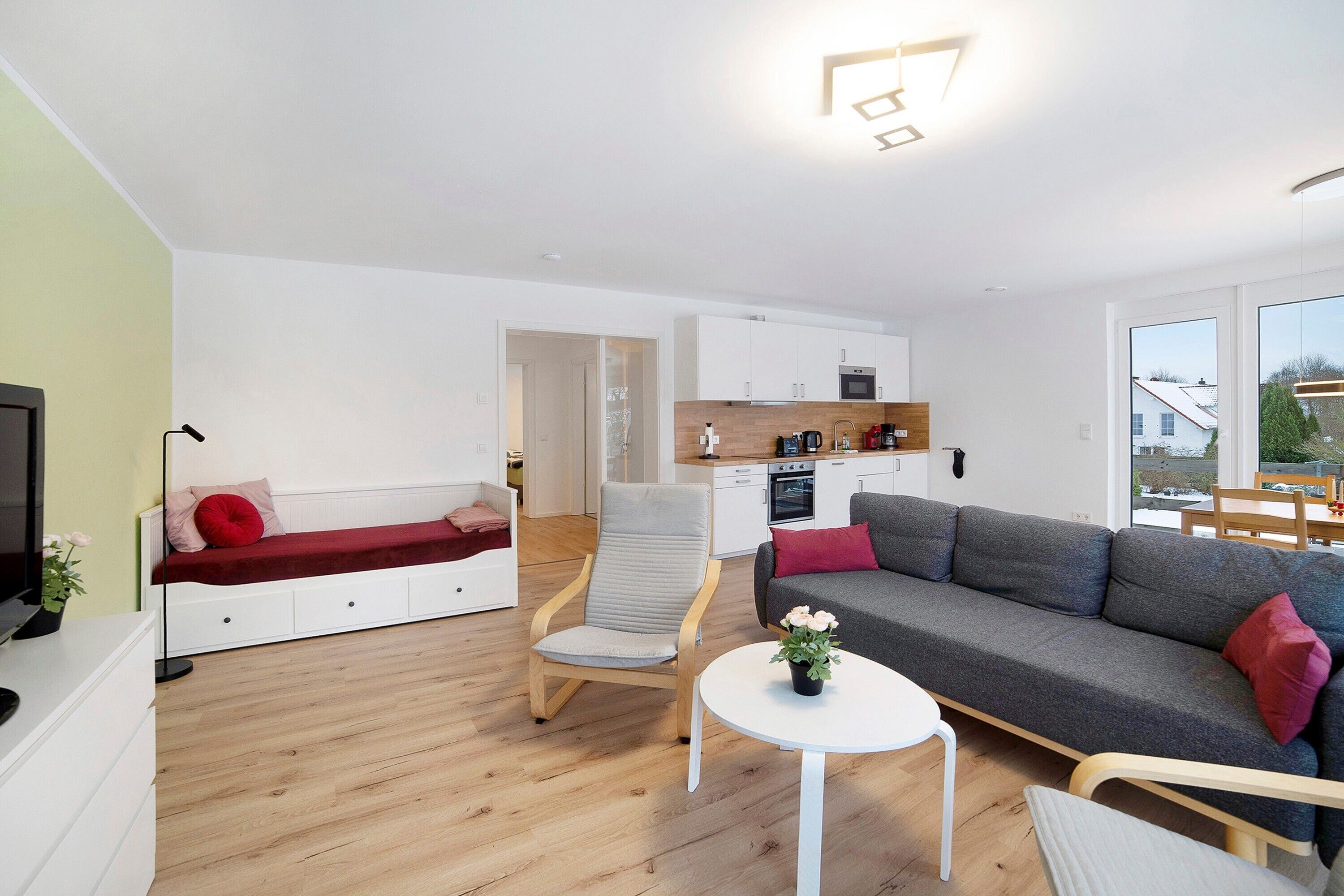 A modern living room with a sofa, a chair, a small table with flowers, and a kitchen area in the background.
