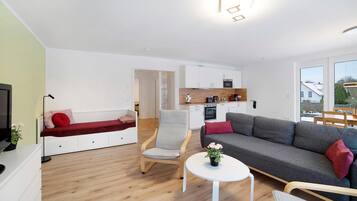 A modern living room with a sofa, a chair, a small table with flowers, and a kitchen area in the background.