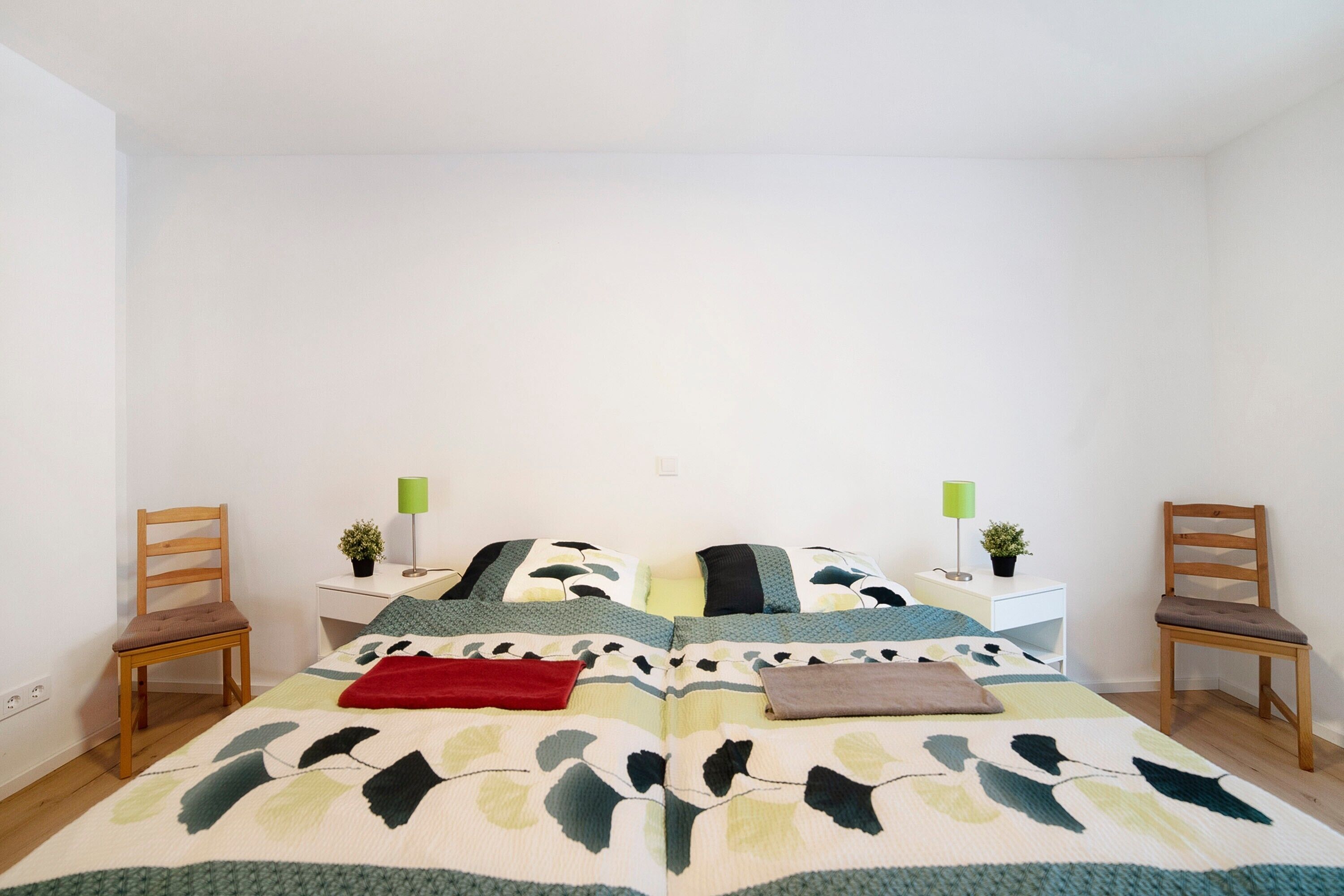 A bedroom with a bed, two nightstands, two chairs, a desk, and a lamp.