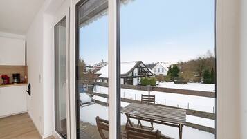 A balcony with a wooden table and chairs, a view of a snowy landscape, and a house in the background.