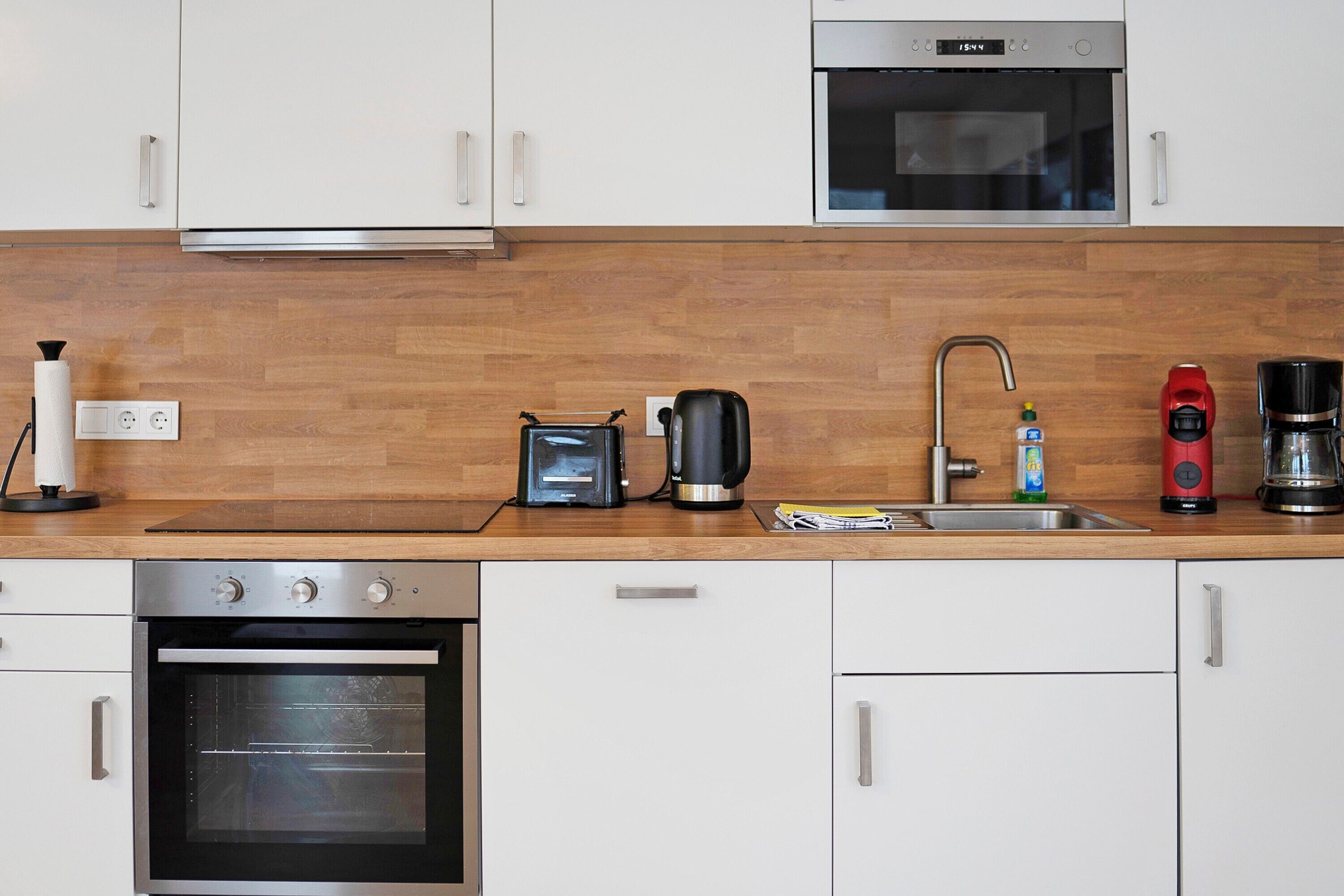 Una cocina moderna con armarios blancos, encimera de madera, horno empotrado, cafetera y tostadora.
