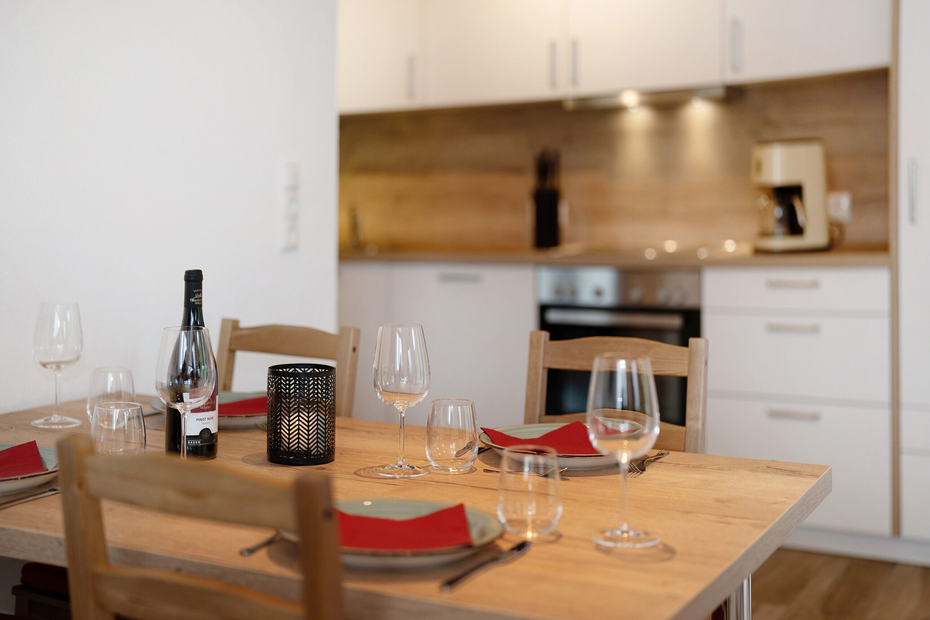 Uma mesa de jantar posta com copos de vinho, pratos e talheres, com uma garrafa de vinho e uma vela sobre a mesa.