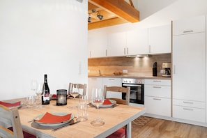 Une cuisine moderne avec des armoires blanches, un plan de travail en bois et une table à manger agrémentée de verres à vin et d’assiettes.