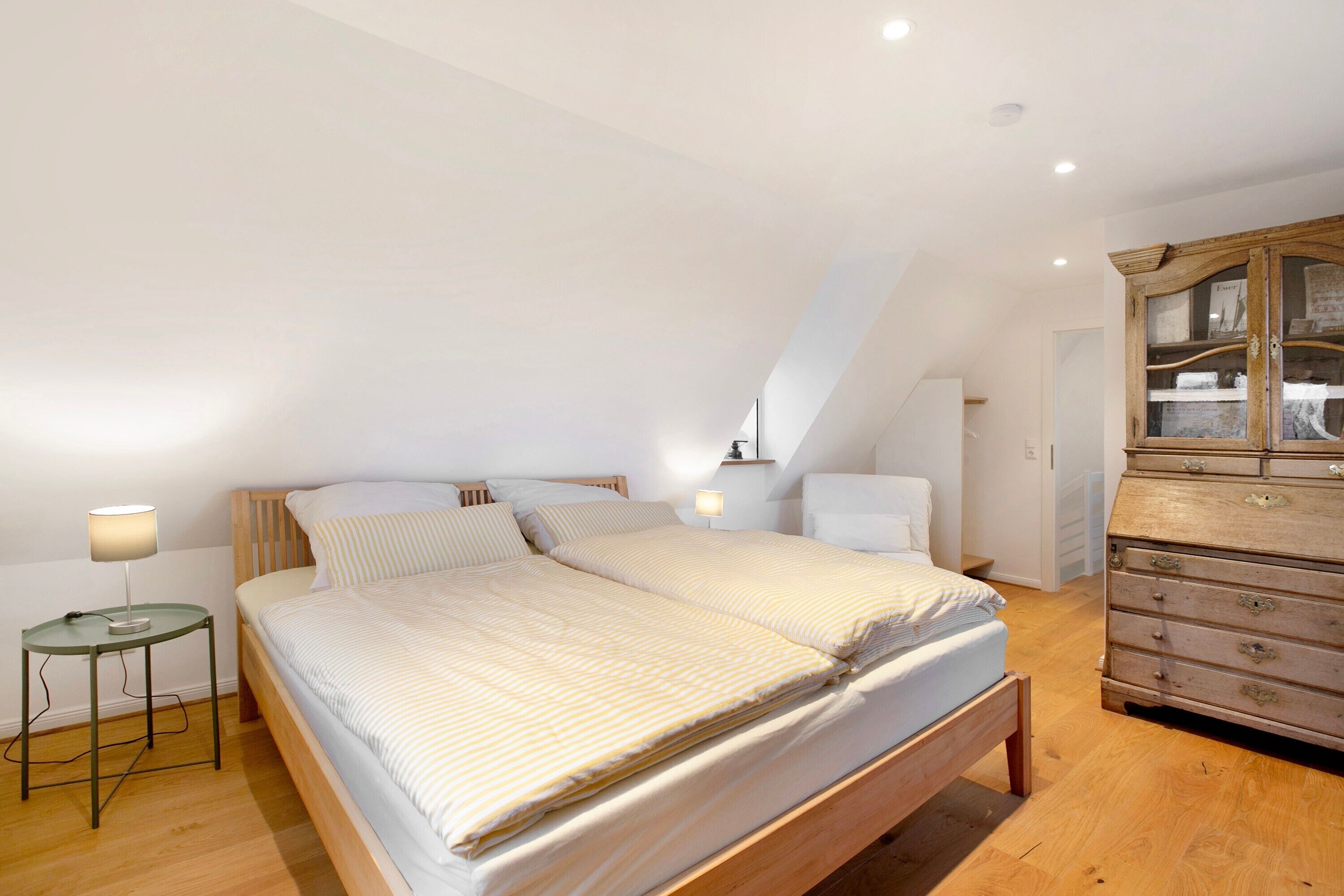 Une chambre à coucher comprenant un lit, une table de chevet, une lampe, une commode et un plafond en pente.