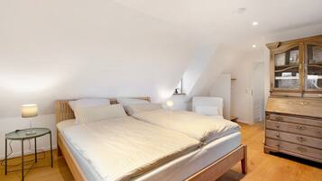 Une chambre à coucher comprenant un lit, une table de chevet, une lampe, une commode et un plafond en pente.