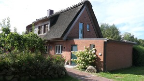 Une maison en briques avec un toit à forte pente, un mur en pierre et un jardin bien entretenu agrémenté de plantes à fleurs.