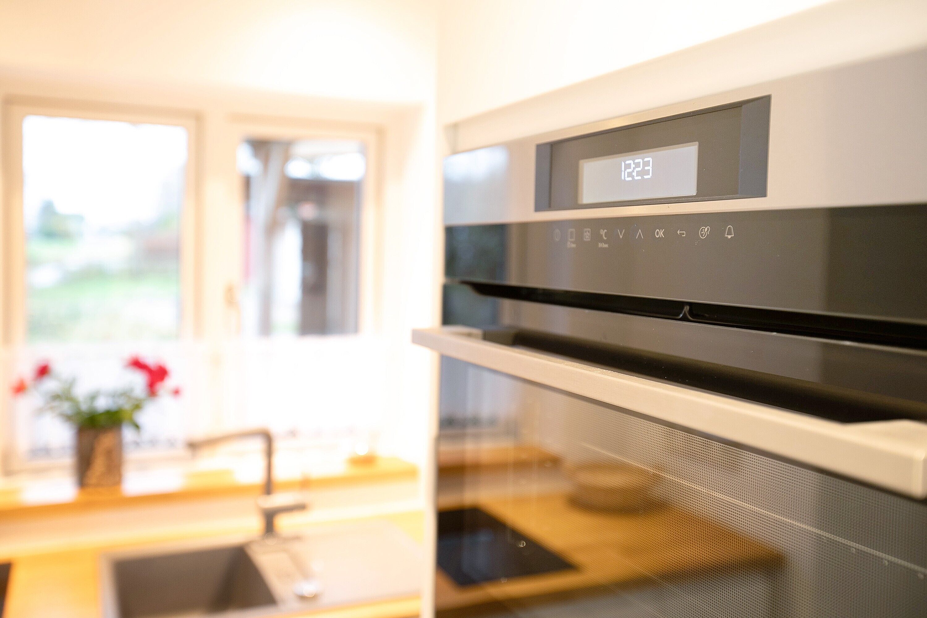 Eine moderne Küche mit digitaler Uhr, einem Edelstahlbackofen und einem Fenster mit Blick ins Grüne.
