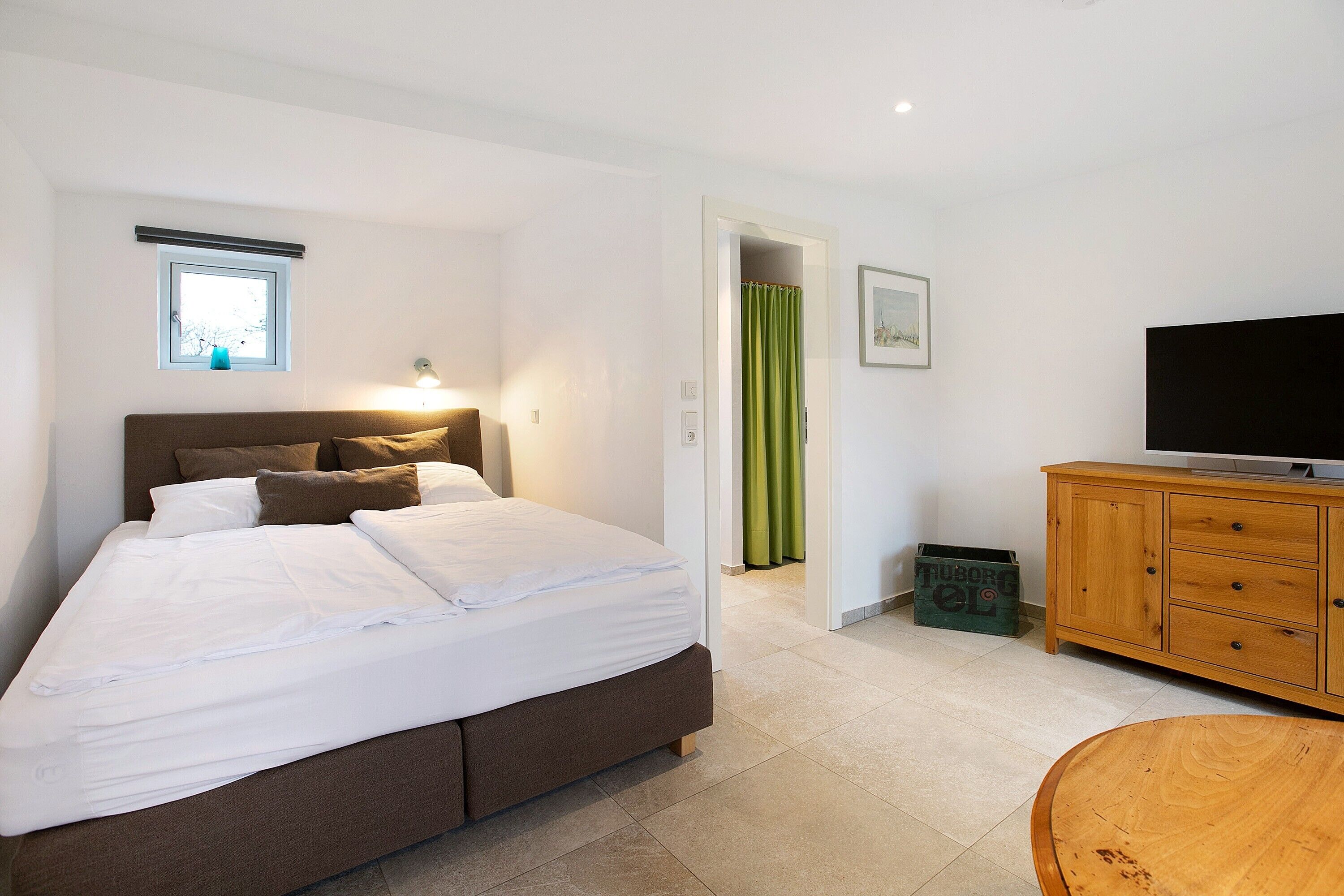 A bedroom with a bed, a television, a wooden cabinet, and a small window.