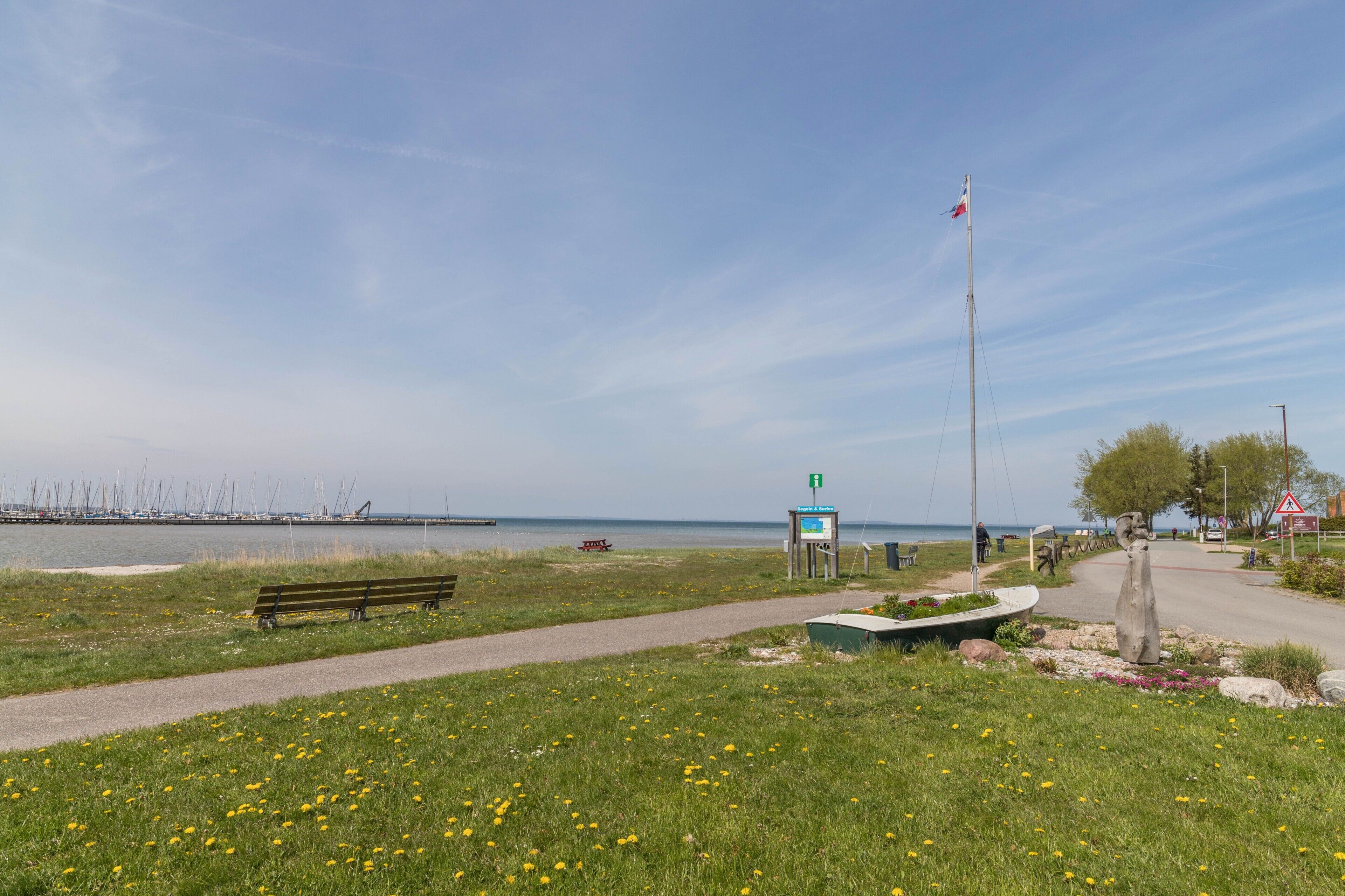 A grassy area with a path, a bench, a boat, and a flagpole.