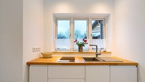 Une cuisine avec une fenêtre, un évier, un vase de fleurs et un panier posé sur le comptoir.