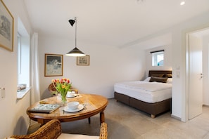 Ein Schlafzimmer mit Bett, Nachttisch, Fenster und einer Essecke mit Tisch und Stühlen.