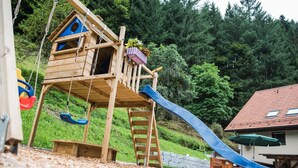 Eine Holzspielkonstruktion mit Rutsche, Schaukeln und einer Kletterleiter.