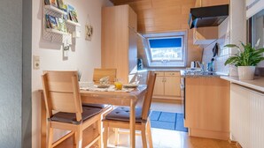 Eine kleine Küche mit Holzausbau, einem Esstisch mit Stühlen, einem kleinen Fenster und einem Blumentopf.