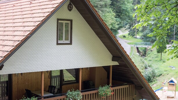 Ein Chalet mit Balkon, Holzterrasse und Blick auf einen bewaldeten Bereich.
