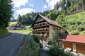 Ein zweistöckiges Gebäude mit einem geneigten Dach, Holzbalkonen mit Bepflanzung und einer Garage mit rotem Dach.