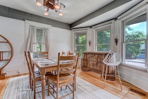 A dining area with a wooden table and chairs, a rustic bar, and large windows with white trim. - Vintage Retreat (Colorado Springs)