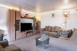 Ein modernes Wohnzimmer mit Flachbildfernseher, Holzschränken, einer Couch und einem Glastisch.