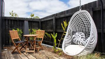 A wooden deck with a hanging chair and two wooden chairs with cushions.