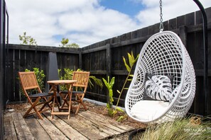 A wooden deck with a hanging chair and two wooden chairs with cushions.