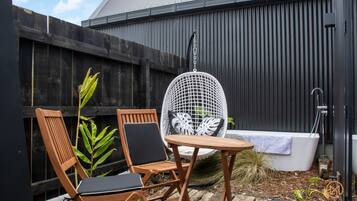 A patio with two wooden chairs, a white mesh chair, and a small table. A white bathtub is visible in the background.
