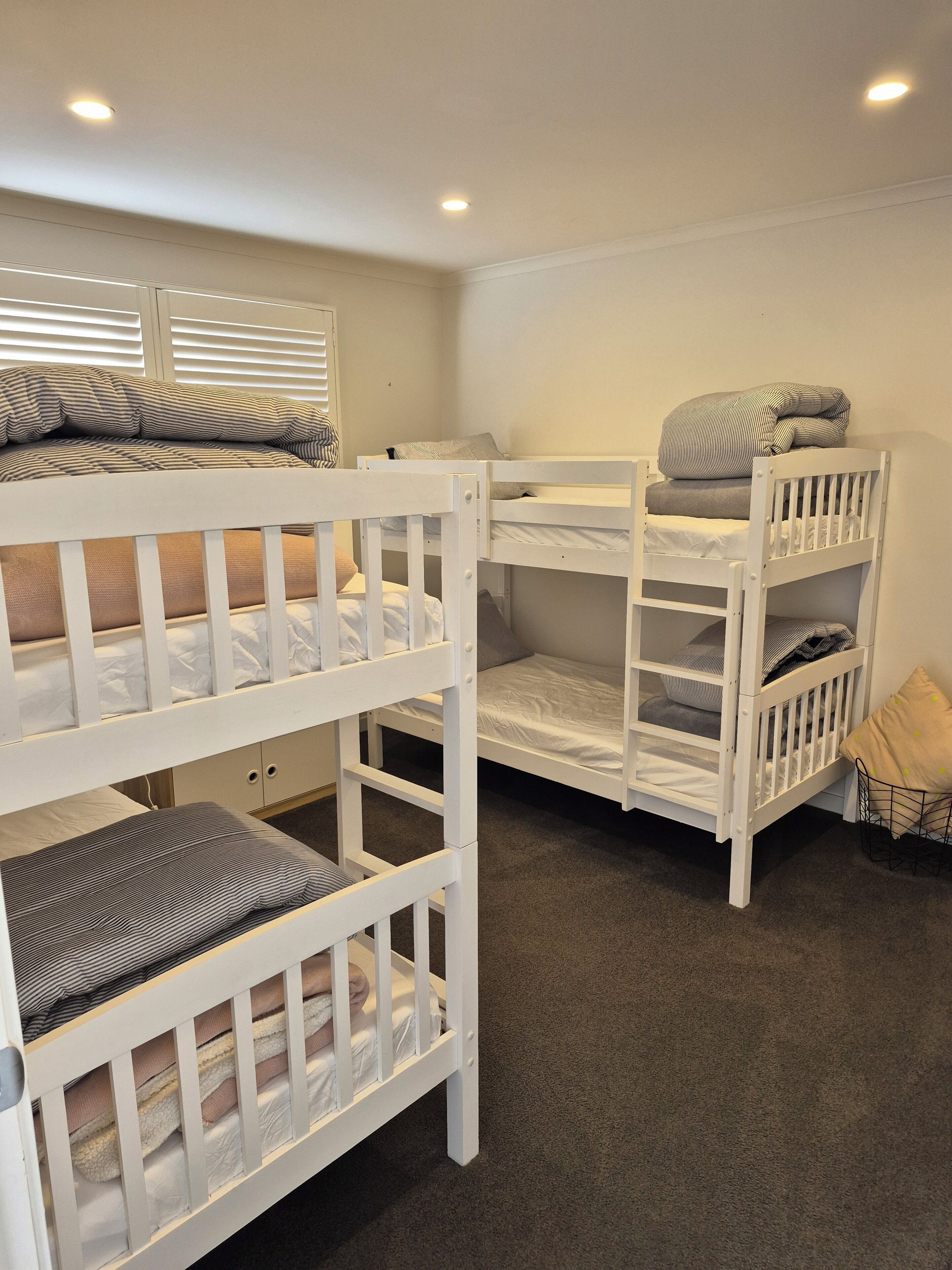 Een slaapkamer met een stapelbed, witte hekken en grijze beddengoed.