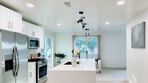 A modern kitchen with stainless steel appliances, a central island, and a large window providing natural light.