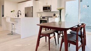 A modern kitchen with white cabinets, stainless steel appliances, a central island with bar stools, and a dining area with wooden chairs.