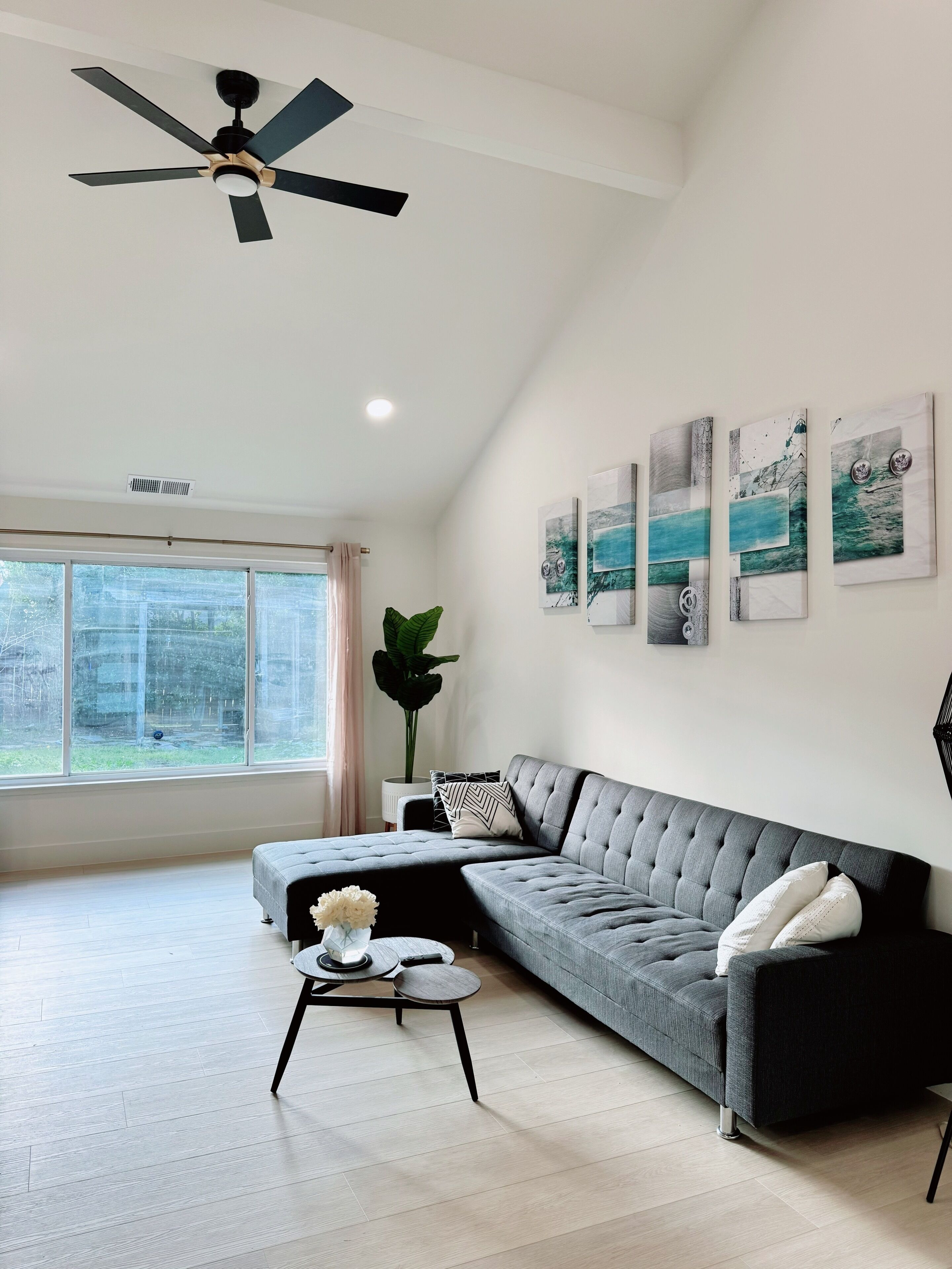 Una sala moderna con un sofá modular gris, una mesa de centro redonda y un ventilador de techo.