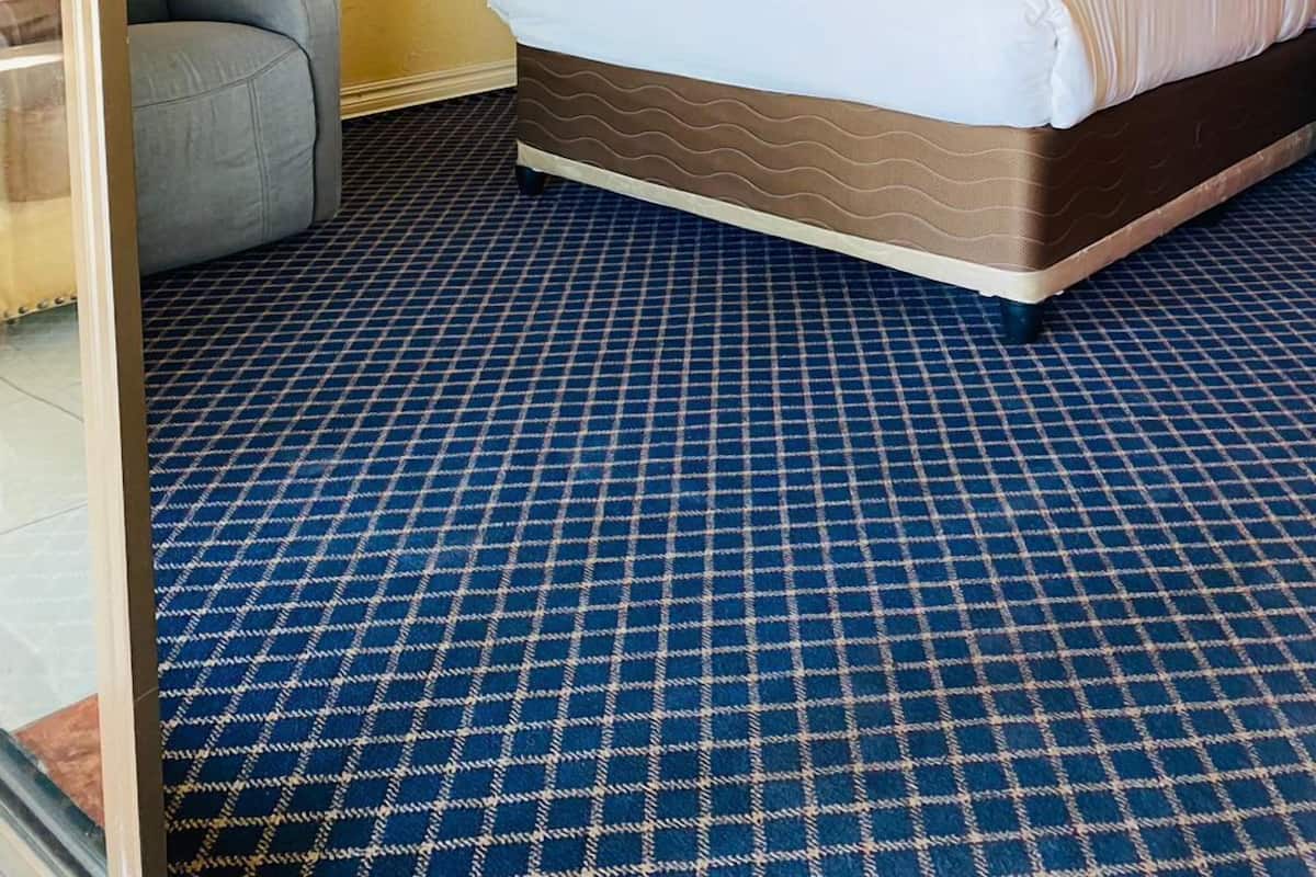 A hotel room with a bed, a chair, a painting on the wall, and a patterned carpet.
