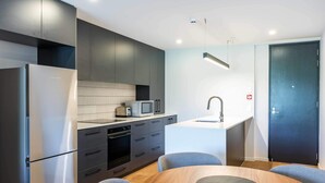 A modern kitchen with a refrigerator, microwave, and stove, a small island with a sink, and two grey chairs around a wooden table.