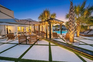 Un espace aménagé au bord de la piscine, avec des meubles en bois et une pergola décorée de guirlandes lumineuses.