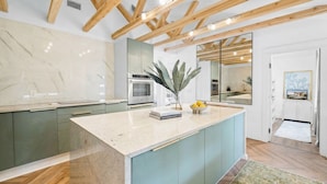 Una cocina moderna con encimera de mármol, armarios verdes, una isla central y vigas de madera en el techo.