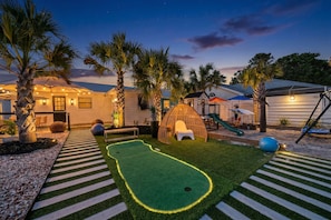 A backyard with a putting green, palm trees, and a swing set.