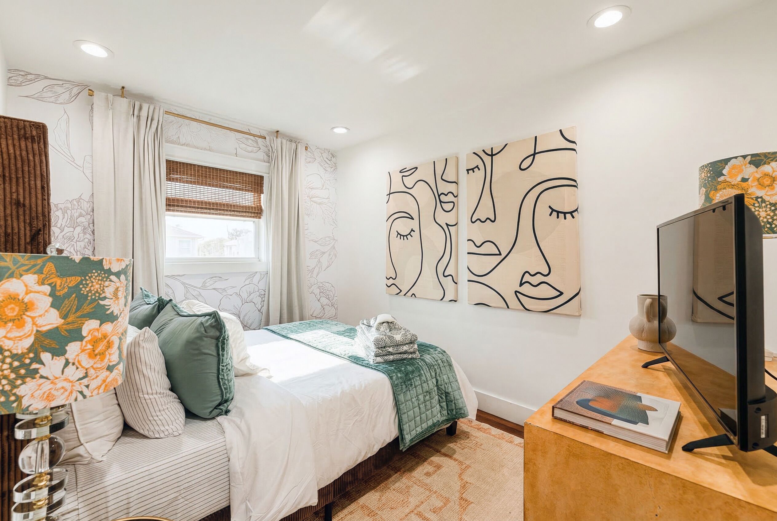 A bedroom with a bed, a desk with a computer, and abstract wall art.