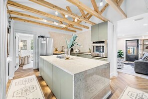 A modern kitchen with a central island, wooden beams, and a dining area with a sofa.