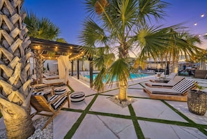 A poolside area with lounge chairs, a pergola with string lights, and a palm tree.