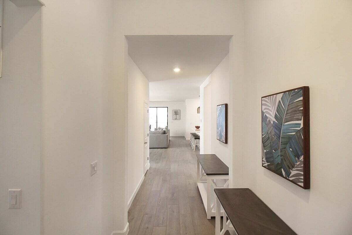 A hallway with a dining area, white walls, and a wooden floor.