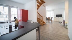A modern kitchen with a central island, a red cabinet, and a wooden staircase leading to a dining area.