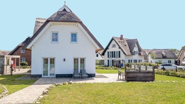 A white house with a steeply pitched roof, a front porch, and a paved driveway.