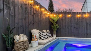 Een achtertuin met een houten omheining, lichtjes, een zwembad, een comfortabele zithoek en potplanten.