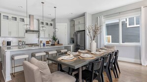 Een moderne keuken met witte kasten, een centraal eiland en een eethoek met een lange tafel en stoelen.