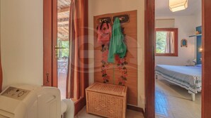 Una habitación con cama, una mesita pequeña, una cesta de mimbre y un cabecero de madera con una toalla colgada.