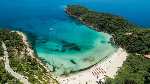 Vista aérea de una zona costera con playa, aguas turquesas cristalinas y una carretera que conduce a la orilla.