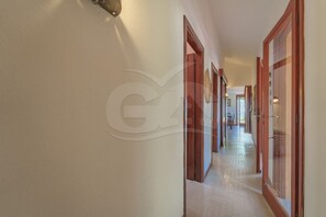 A hallway with wooden doors and a tiled floor, leading to a room with a window.