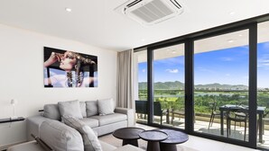 Een moderne woonkamer met een grijze bank, twee ronde salontafels en een groot raam met uitzicht op een rivier en heuvels.