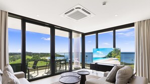 Een moderne woonkamer met een grote televisie, comfortabele zitmogelijkheden en uitzicht op de oceaan.