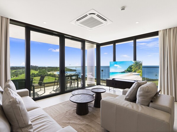 A modern living room with a large TV, comfortable seating, and a view of the ocean.