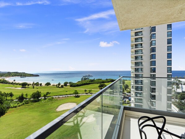 A balcony with a clear view of a beach, ocean, and a high-rise building.
